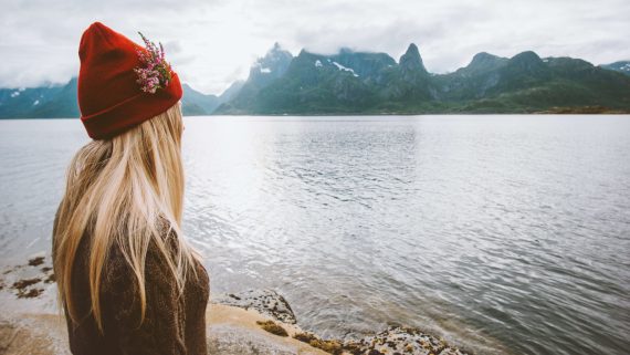 Woman traveling solo in Norway outdoor summer vacation healthy lifestyle blonde hair girl in red hat and flowers enjoying view of Lofoten islands